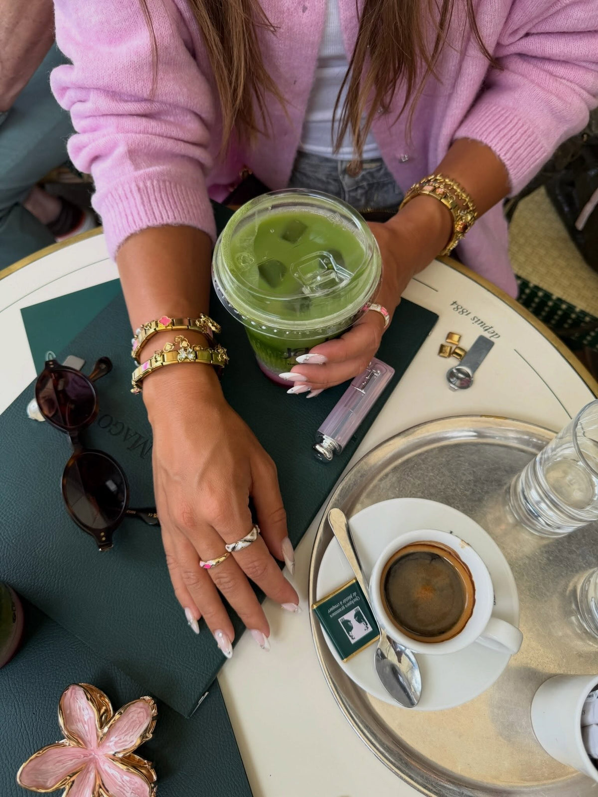Main portant plusieurs bracelets à charms italiens dorés, posée près d’un matcha
